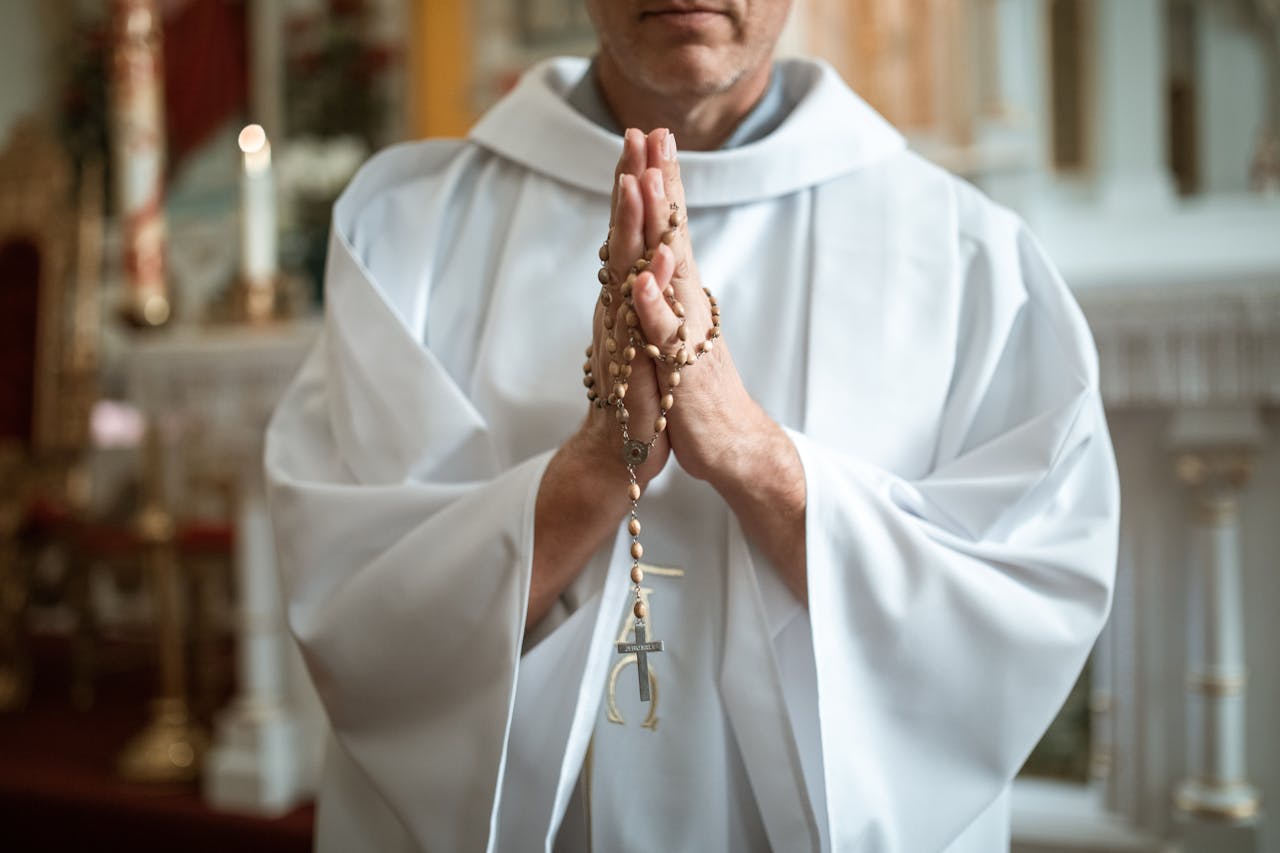A Catholic priest holding rosary beads in prayer inside a church.