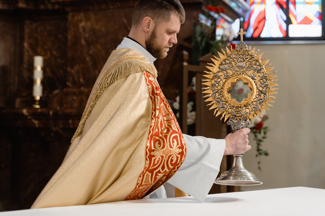 Priest in ornate vestments holding a monstrance during a religious ceremony inside a church.