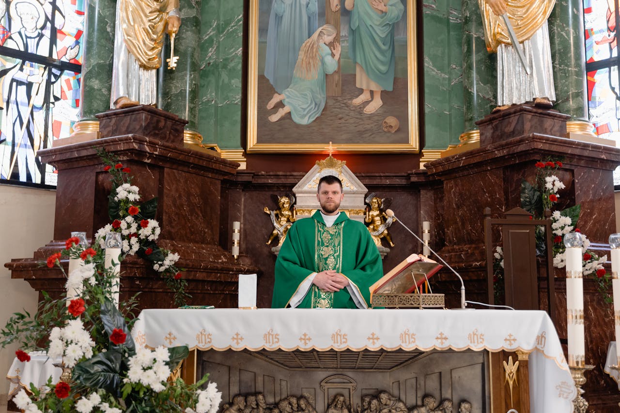 A Catholic priest in green vestments stands solemnly at the altar in a beautifully adorned church.