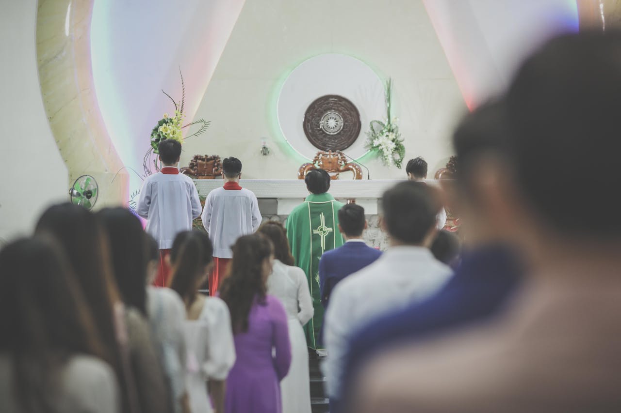 A group of people participating in a Catholic mass ceremony in a church, led by a priest in green vestments.